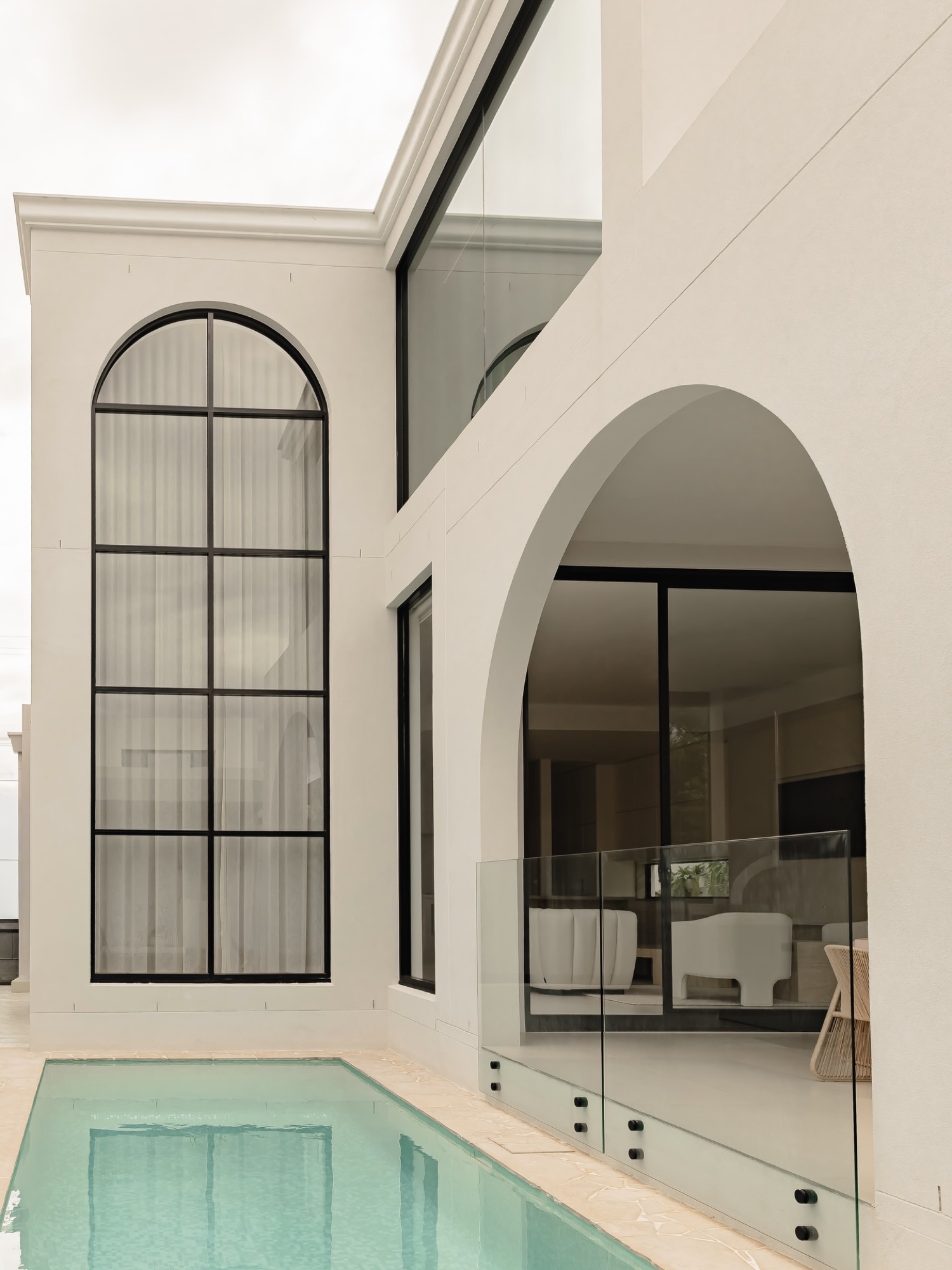 Pool courtyard framed by a tall arched opening and steel window